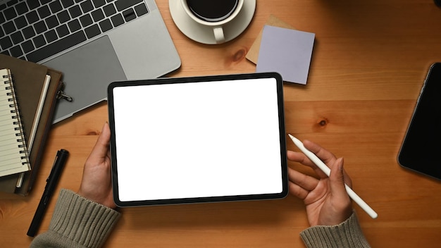 Creative woman hands holding digital tablet with white empty display over wooden working desk