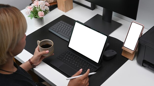 Creative woman holding coffee cup and working with digital tablet in office.