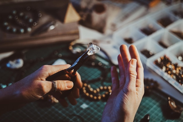 creative woman is holding pliers and crystal clear quartz in it.