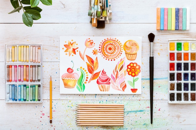 Creative work desk with paint brushes on white wooden background, flat lay