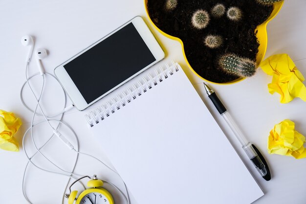 Creative work place with mobile phone headphones notebook with copy space, alarm clock and cactus. Work from home concept. Online education. Top view. Flat lay.