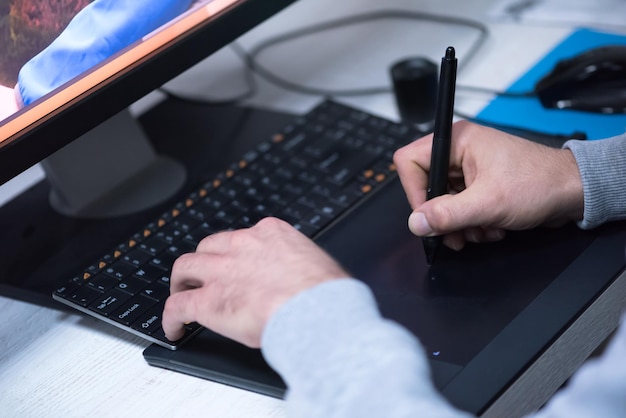 creative worker, photo editor working on graphic tablet at his desktop computer at small startup office