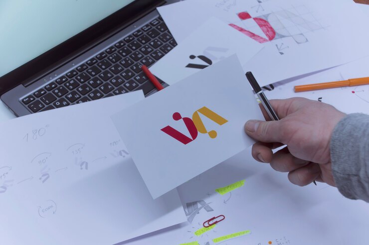 Creative workplace of a Graphic Designer. A man in the office is developing a logo on the table against the background of printed sketches and a laptop.