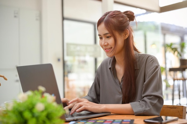 彼女の仕事に取り組んでいて、ポータブルラップトップを使用している創造的な若いアジアの女性のグラフィックデザイナー