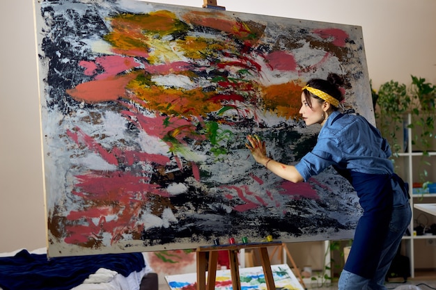 Creative young female painter working on a large modern abstract oil painting applying paint on