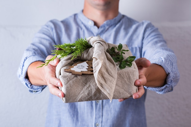 Creative zero waste Christmas concept. Hands giving handmade gift box wrapping in eco friendly traditional Japanese style furoshiki fabric