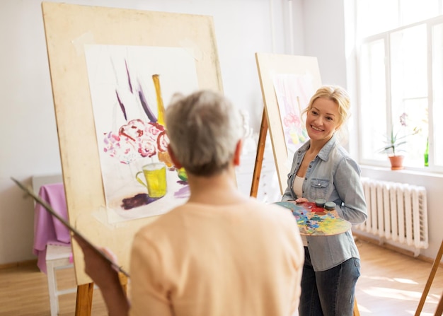 creativiteit, onderwijs en mensenconcept - vrouwelijke kunstenaars schilderen stilleven op easels in de studio van de kunstacademie en praten