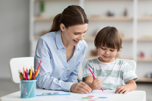 Creativiteitslessen voor kinderen, gelukkig jongetje tekenen met professionele vrouwelijke leraar bij