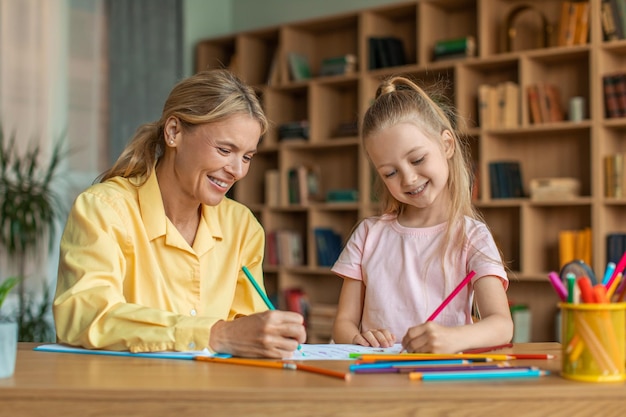 Creativiteitslessen voor kinderen Gelukkig meisje tekenen met professionele vrouwelijke leraar bij kabinet genieten van kunstlessen