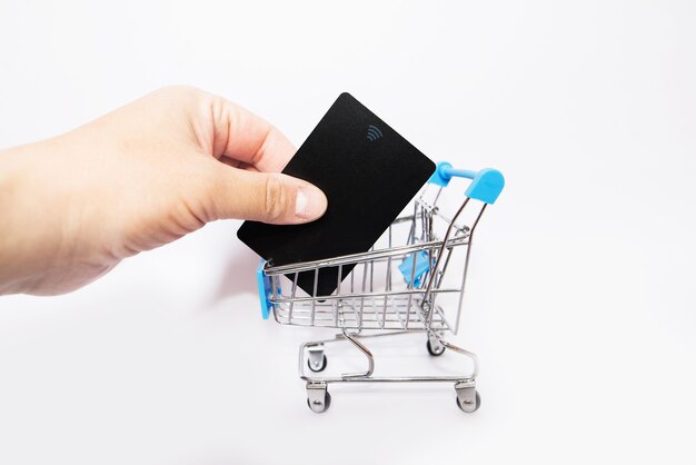 Credit card in hand and a small shopping trolley on a white background