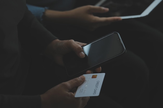 A credit card in the hands of a young businesswoman pays for a business on a mobile phone and on a desk with a laptop