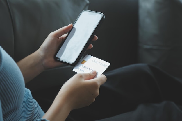 A credit card in the hands of a young businesswoman pays for a business on a mobile phone and on a desk with a laptop