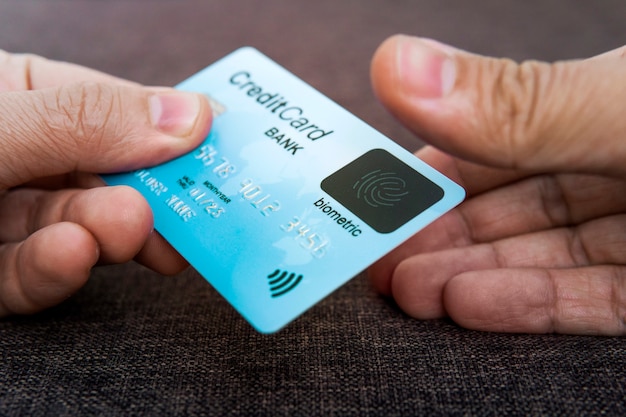 Credit card has built-in fingerprint scanner. Illustration of biometric payment security. One male hand is holding blue card and other touching scanner with thumb. Verifying by pressing. Identity.