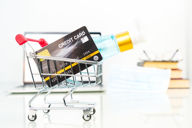 Credit card in shopping cart front of laptop screen with alcohol gel bottle