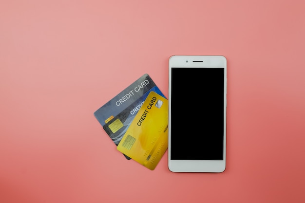 Credit card and smart phone with copy space on light pink background, Top view