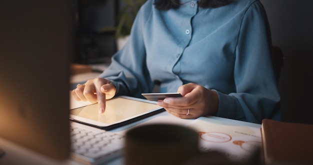 Photo credit card tablet and online shopping with a business woman in office at her desk late in the night hands finance and payment with a female employee making a purchase while working overtime