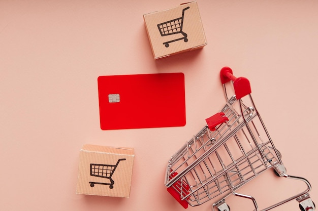 Credit card with shopping cart and delivery boxes on pink background closeup Shopping and delivery