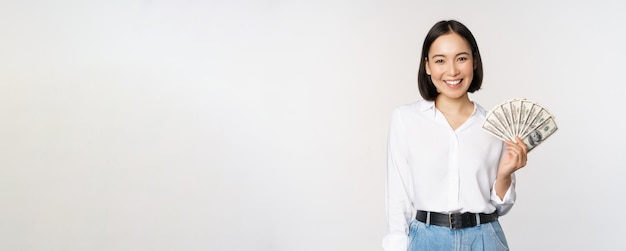 Credit and loan concept Smiling young asian woman holding cash dollars and looking happy at camera white background