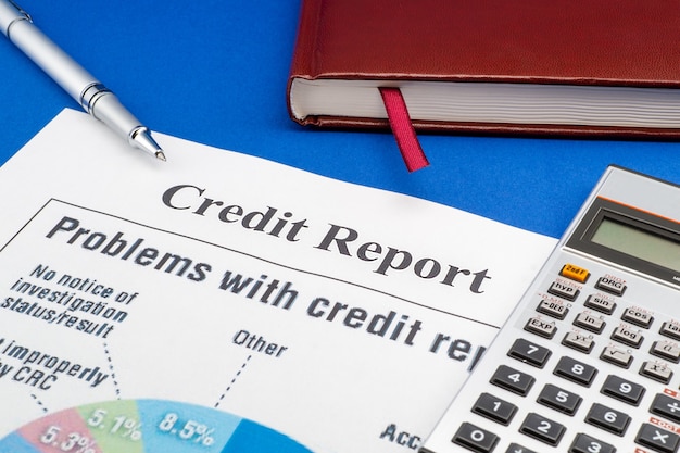 Credit report on the blue table, pen, notebook and calculator.