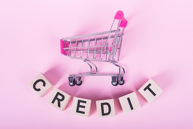 CREDIT word on wooden cubes on a pink background with a shopping trolley