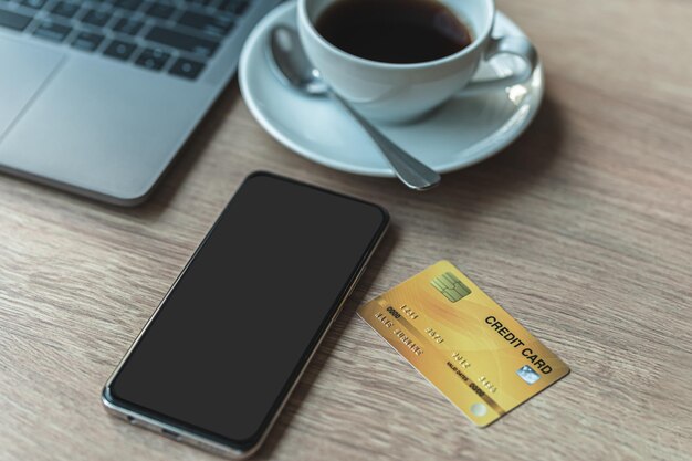 Creditcard van laptopcomputer, smartphone grijs zwart leeg scherm en koffiekopje op houten achtergrond, online bankieren concept