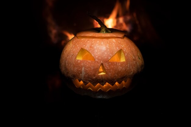 Raccapricciante zucca di halloween vicino a un camino. fuoco sullo sfondo.