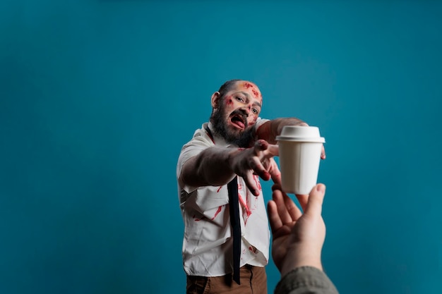 Creepy horror devil wanting cup of coffee, chasing after hand with carton cup with drink. Aggressive scary zombie eating brain and looking dangerous with bloody scars or wounds.