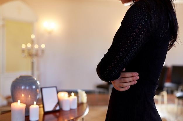 Photo cremation, people and mourning concept - close up of woman with cinerary urn and photo frame at funeral in church