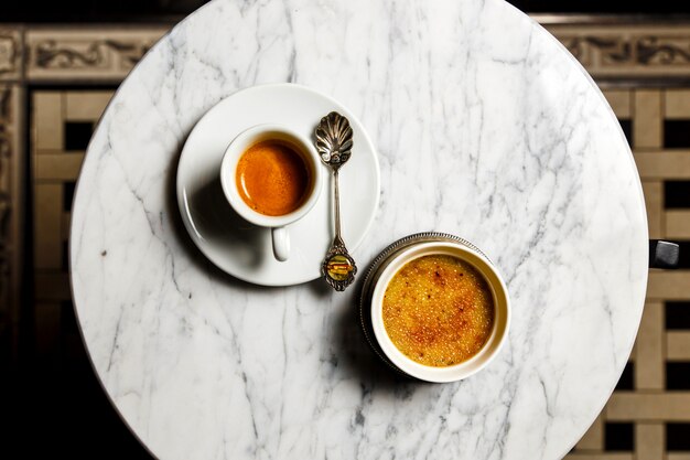 Crème brulée dessert e una tazza di caffè espresso con un bellissimo vecchio cucchiaio su un tavolo di marmo, vista dall'alto