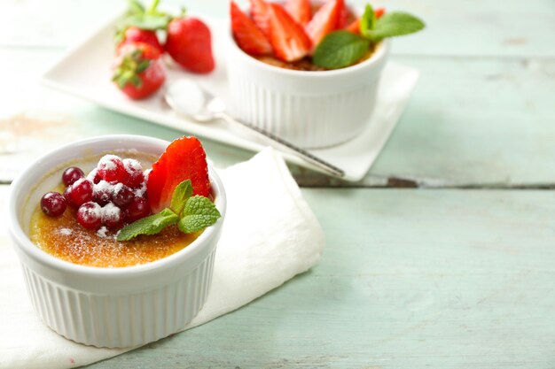 Creme brulee dessert with fresh strawberry berries on napkin on color wooden background