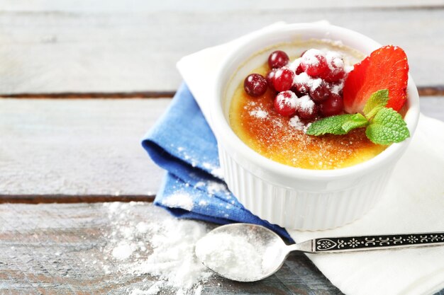 Creme brulee dessert with fresh strawberry berries on napkin on color wooden background