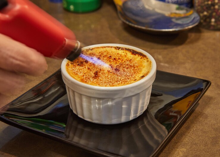 Photo creme brulee with mushrooms in special form, the chef burns sugar with burner. french gourmet cuisine.