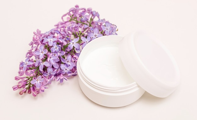 Crème in een pot op een witte achtergrond en lila bloemen. Huidverzorging, gezondheidszorg, spa
