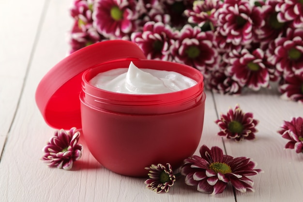 Crème in een rode pot close-up en bloemen van chrysanthemum op een witte houten tafel.