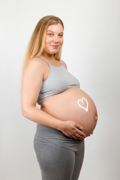 Crème op de buik van een zwanger meisje in de vorm van een hart Huidverzorging voor een zwangere vrouw