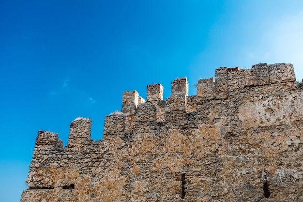 Photo crenellated fortress wall made of old stone, against sky, view from below.