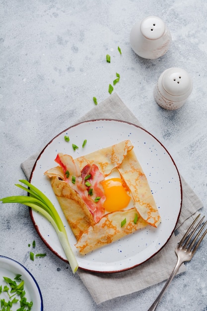 밝은 회색 콘크리트 표면에서 아침 식사로 계란, 치즈, 베이컨, 파를 곁들인 크레이프