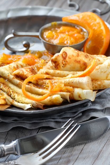 Crepes Suzette on vintage metal plate on wooden table served with orange sauce