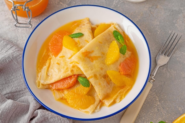 Crepes suzette with orange syrup and slices fruits on a plate on a gray concrete background