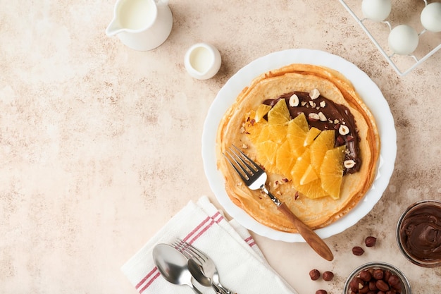 Crepes suzette with oranges Thin crepes with chocolate spread hazelnuts and orange slices fruit in white plate for breakfast on old concrete rustic table background Copy space Top view