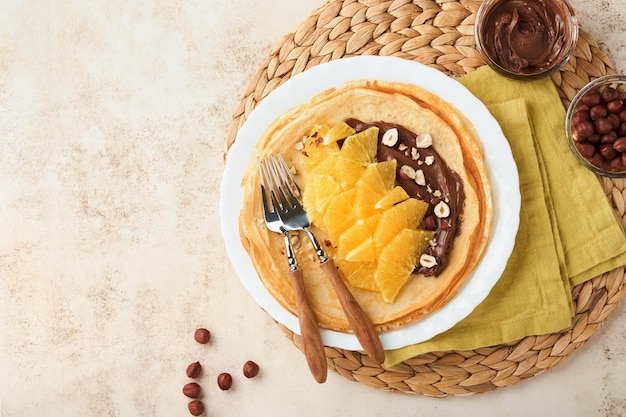 オレンジのクレープシュゼットチョコレートスプレッドヘーゼルナッツとオレンジスライスフルーツの薄いクレープは、古いコンクリートの素朴なテーブルの背景に朝食用の白いプレートにフルーツ