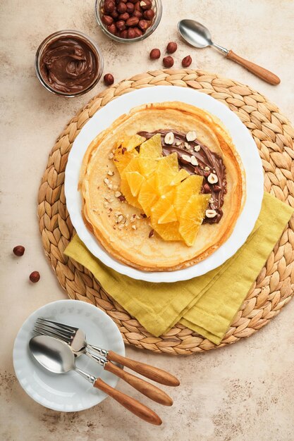 Crepes suzette with oranges thin crepes with chocolate spread\
hazelnuts and orange slices fruit in white plate for breakfast on\
old concrete rustic table background copy space top view