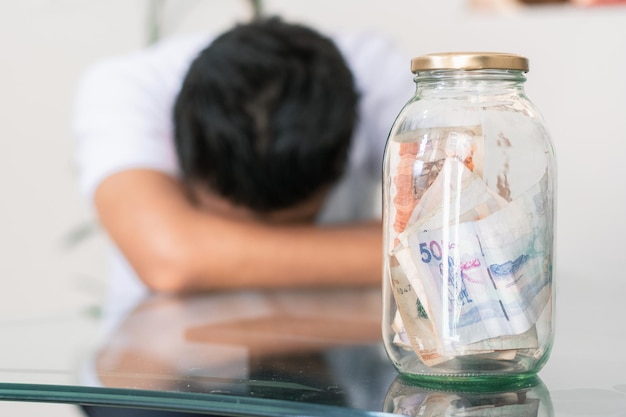 Crestfallen jonge man met zijn spaargeld in een glazen pot op de tafel bankbiljetten in een glazen pot