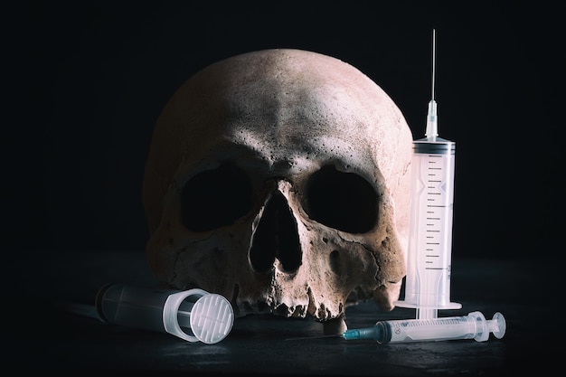 犯罪と麻薬の概念。暗い背景に注射器で人間の頭蓋骨。