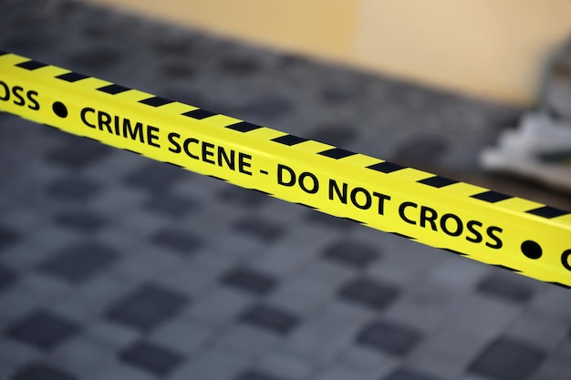 Crime scene tape for covering the area cordon yellow tape with\
blurred forensic law enforcement background in cinematic tone