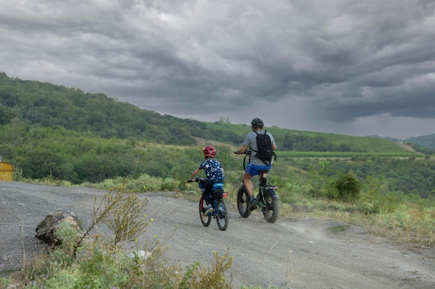 Crimea Ukraine July 30 2021 Dad and son ride mountain bikes in the Crimean mountains against the backdrop of a stormy sky