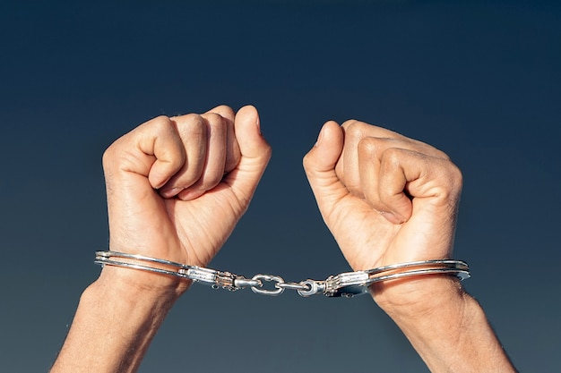 Criminal hands locked in handcuffs. Close-up view