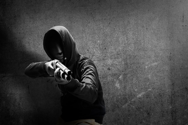 Criminal man in hidden mask pointing the shotgun with black wall background