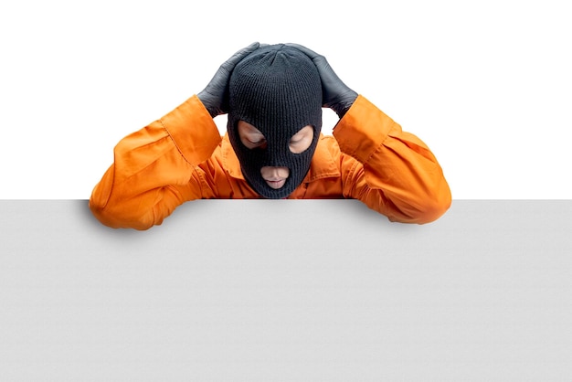 A criminal man in a hidden mask standing behind a white wall isolated over white background