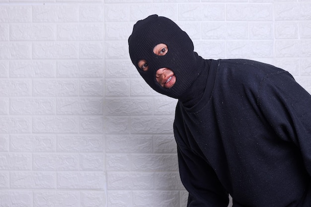 A criminal wearing black balaclavausing torch and peeking out from white wall